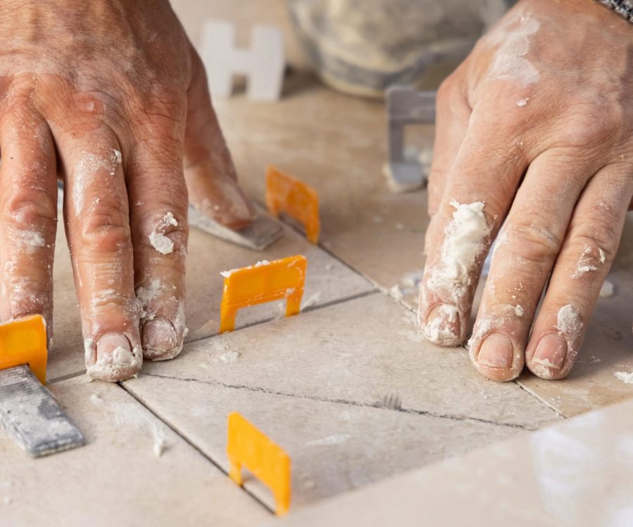 Tiler laying the ceramic tile on the floor with dusty hands closeup. Ceramic tiles and tools for tiler. Professional craftman during home renovation or construction new house